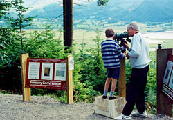 a voluntary RSPB warden helps a young visitor to see the ospreys
